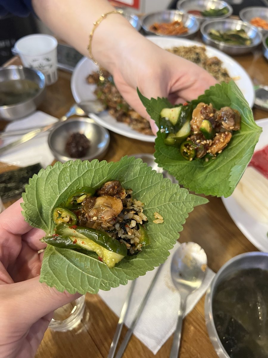 깻잎 쌈 두 개 — 한 장에는 꼬막비빔밥·꼬막·오이무침·고추를, 다른 한 장에는 꼬막·오이무침·고추를 얹었다 (2026년 9월 12일 독도네 본점)