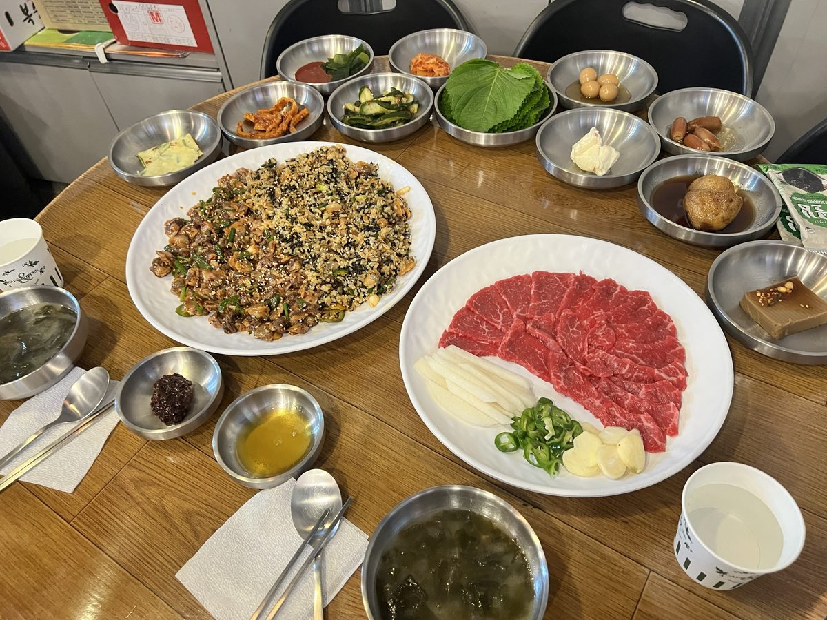 독도네 본점 식탁 — 반은 꼬막무침, 반은 비빔밥인 꼬막비빔밥 한 접시와 부채꼴로 편 육사시미 1/2 접시, 깻잎·오이무침·김치·메추리알·도토리묵 반찬과 미역국 (2026년 9월 12일 직접 촬영)