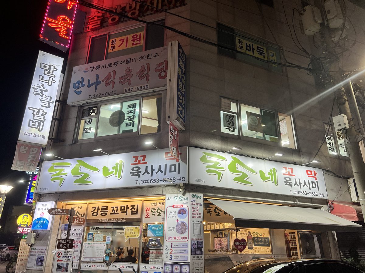 밤의 독도네 본점 앞 — 「독도네 꼬막 육사시미」 간판과 「강릉꼬막집」 간판 (2026년 9월 12일 직접 촬영)