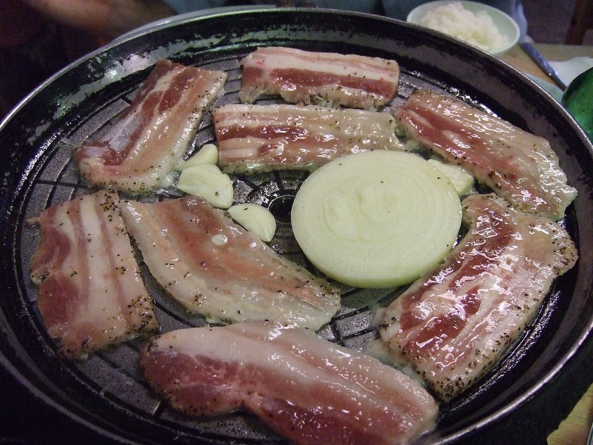 불판 위에 올린 삼겹살과 마늘, 양파 — 위키미디어 공용 사진